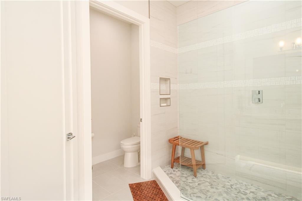 Full bathroom featuring baseboards, tiled shower, toilet, and tile patterned floors