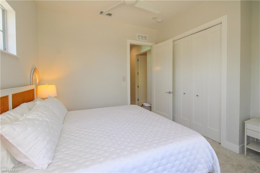 Bedroom with light carpet, ceiling fan, visible vents, and a closet