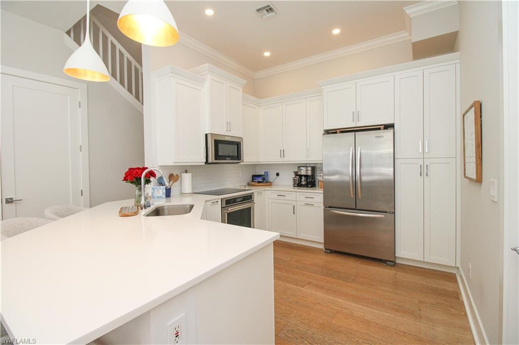 Kitchen featuring stainless steel appliances, visible vents, white cabinetry, hanging light fixtures, and light countertops