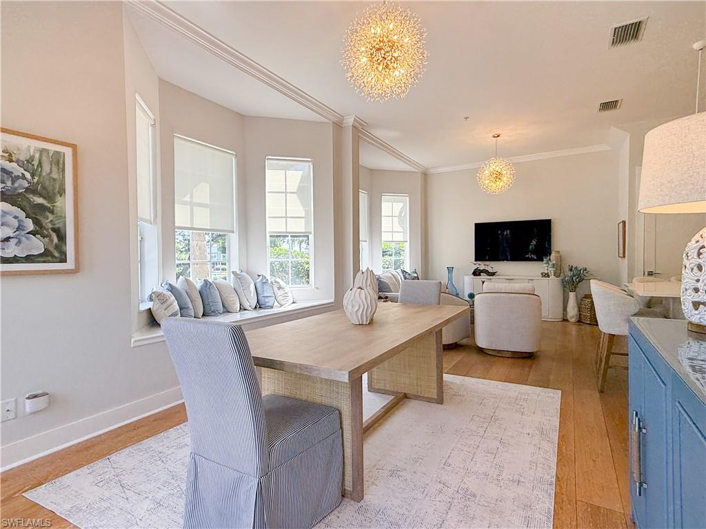 Dining room featuring crown molding, light wood-style floors, visible vents, and an inviting chandelier