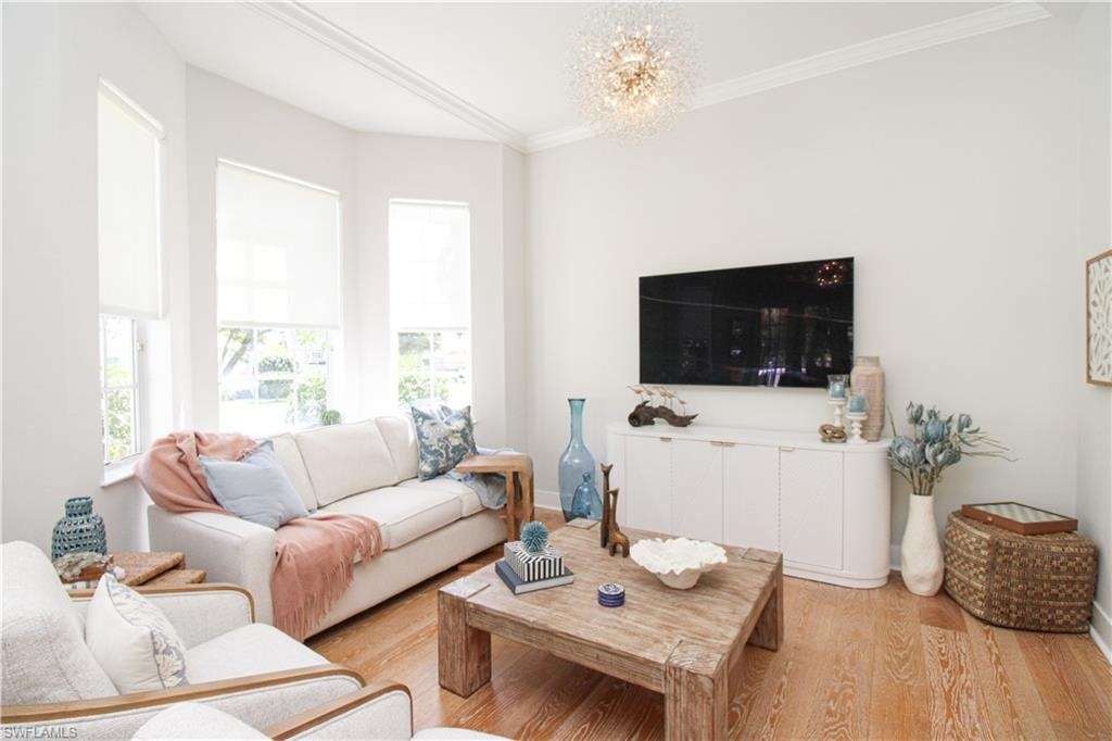 Living room with a notable chandelier, ornamental molding, baseboards, and light wood-style floors