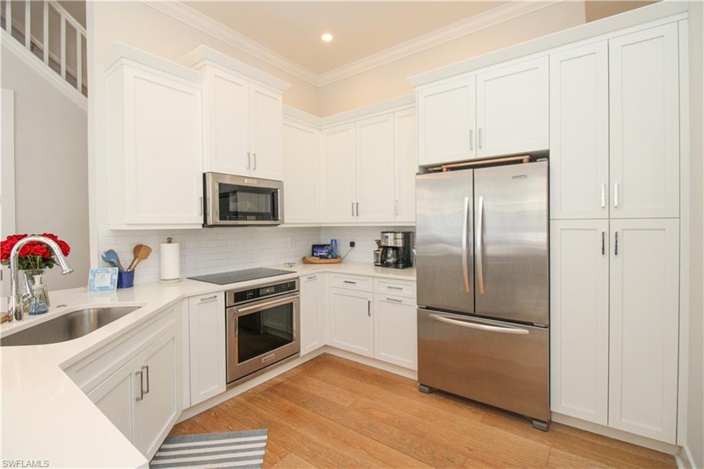 Kitchen with white cabinets, stainless steel appliances, a sink, and light countertops
