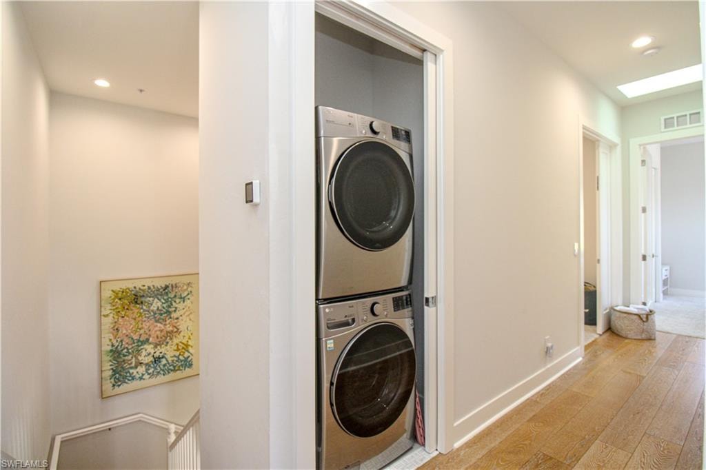 Clothes washing area featuring light wood finished floors, laundry area, visible vents, stacked washer and clothes dryer, and recessed lighting