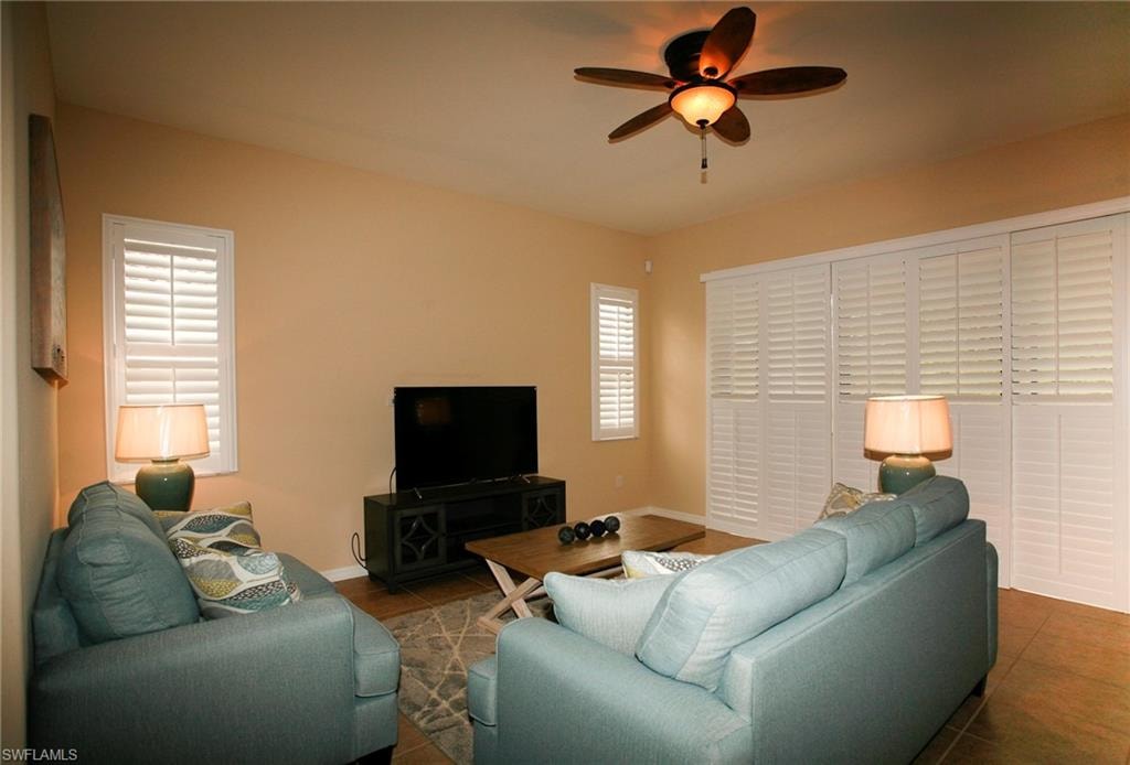 Spacious living room featuring warm neutral walls, wood-finish flooring, dual upholstered seating areas, ceiling fan with integrated lighting, and plantation shutters on expansive windows
