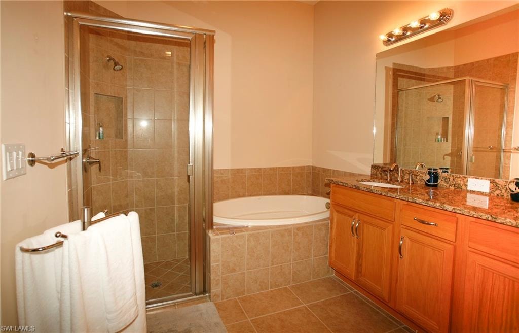 Recessed tub, tiled walk-in shower with glass enclosure, dual vanity with wood cabinetry, and a granite-finish countertop