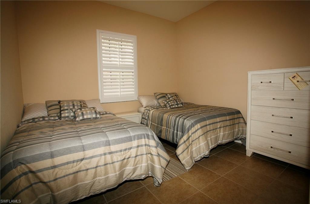 Neutral wall paint, tile flooring, and a window with white louvered shutters