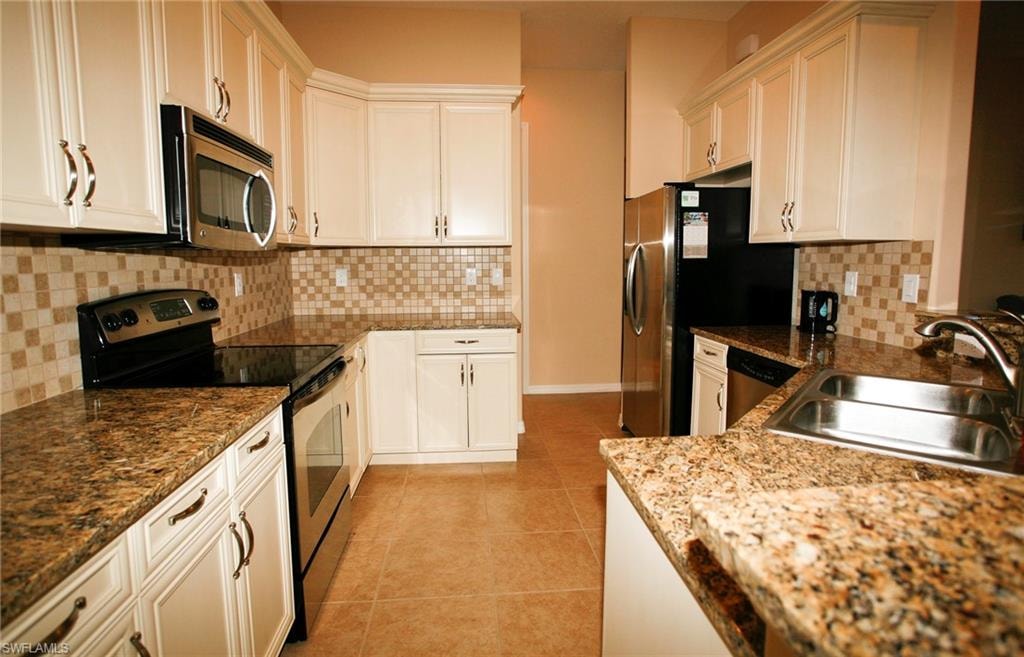 White cabinetry with curved hardware, patterned tile backsplash, stainless steel appliances, and a double basin sink