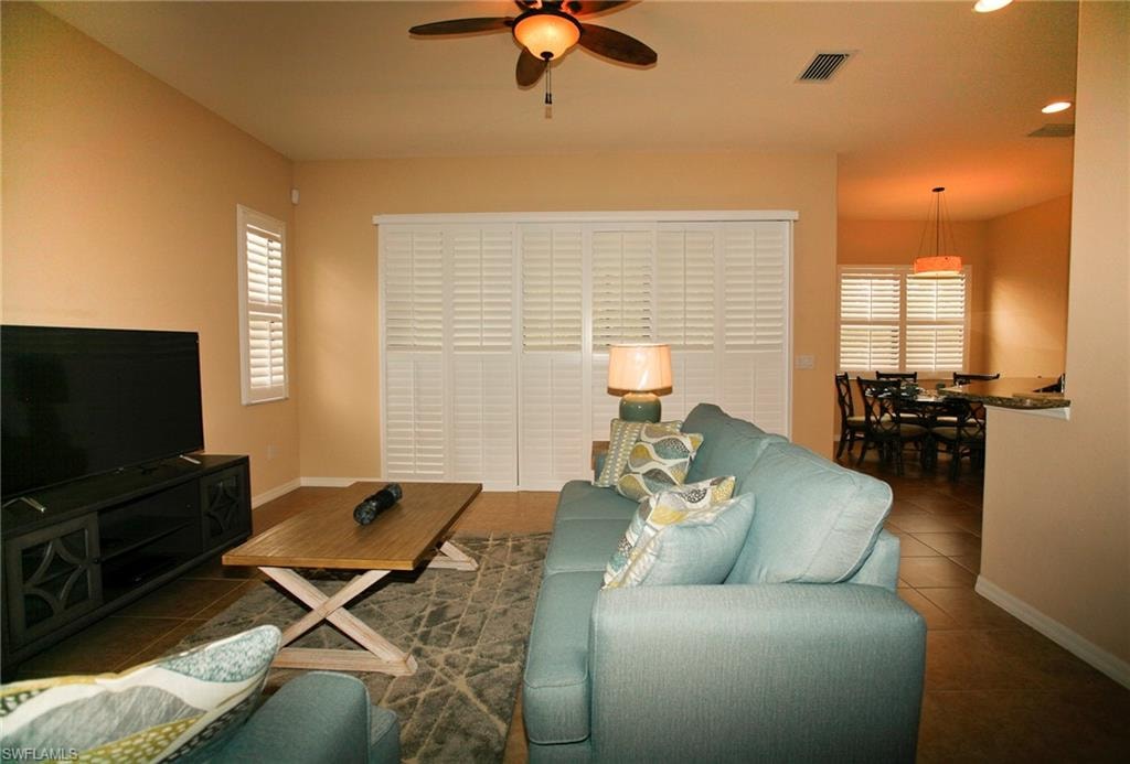 Bright and open living area featuring warm wood-finish flooring, a ceiling fan with integrated lighting, and large plantation shutters framing the primary windows