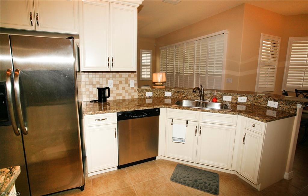 Kitchen featuring granite countertops, stainless steel appliances, white cabinetry, tile flooring, and plantation shutters