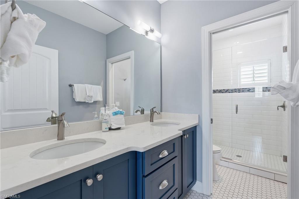 Dual basin vanity with stone countertop, brushed nickel fixtures, glass-enclosed shower, white subway tile surround, and hexagonal floor tile - Virtually Edited Image