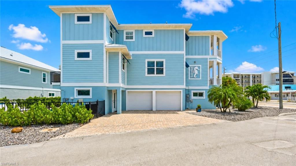 Multi-story residence featuring light blue siding, white trim, a paver driveway, an integrated two-car garage, and established landscaping - Virtually Edited Image