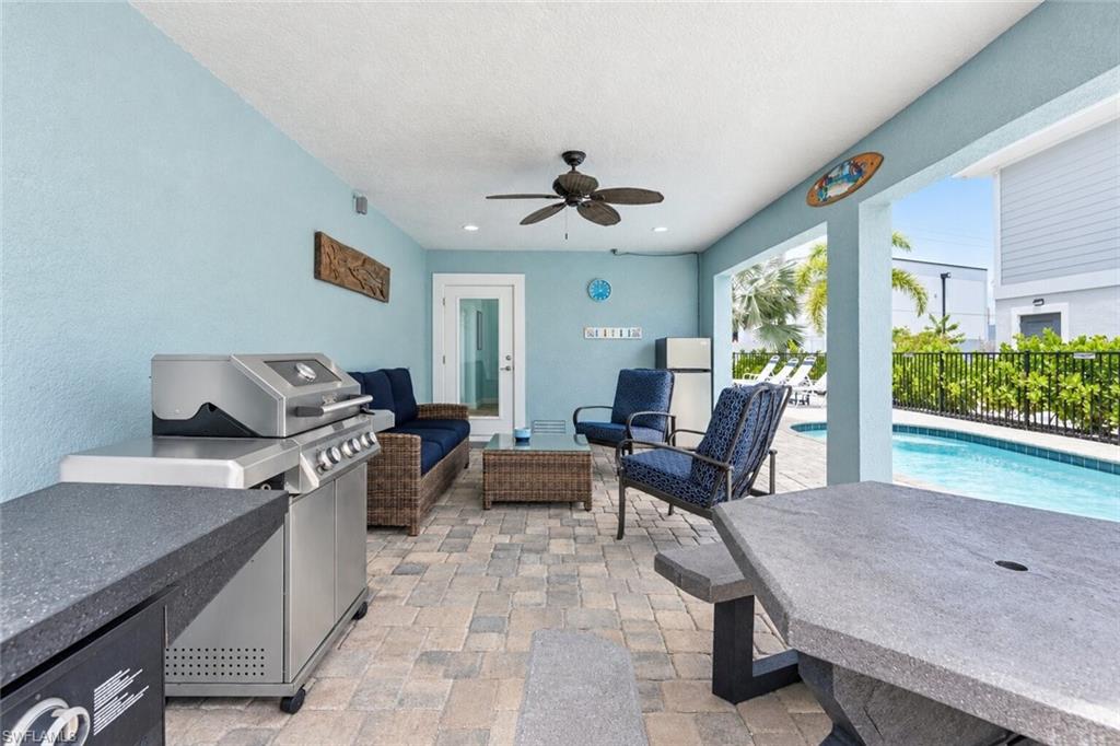 Covered patio with paver flooring, built-in outdoor grill station, ceiling fan, and access to a fenced pool area - Virtually Edited Image