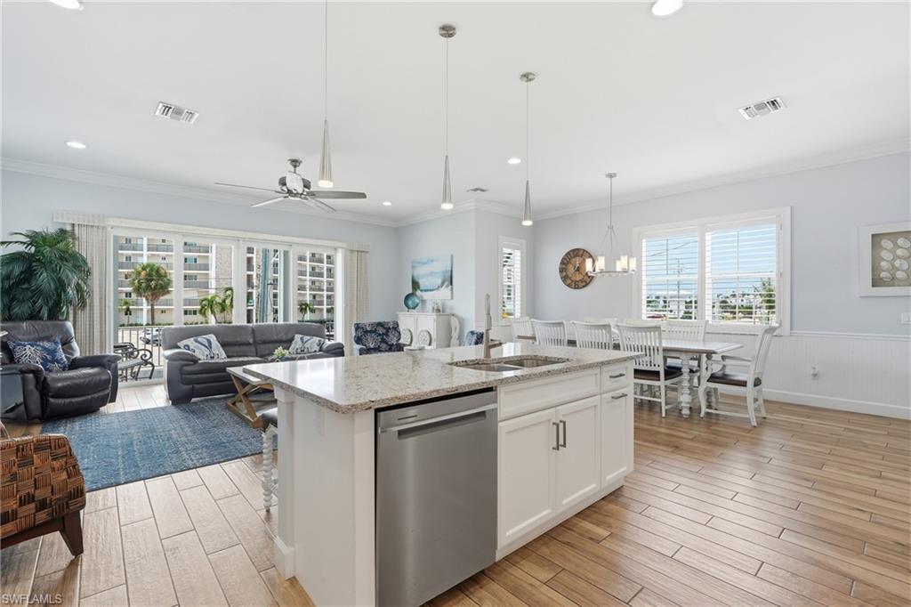 Open-concept living space featuring wood-finish flooring, a kitchen island with stone countertop, stainless steel dishwasher, and white cabinetry - Virtually Edited Image