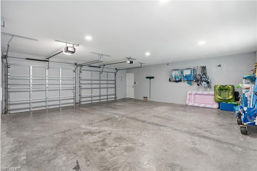 Two-car garage featuring a concrete floor, two automatic garage door openers, and recessed lighting - Virtually Edited Image
