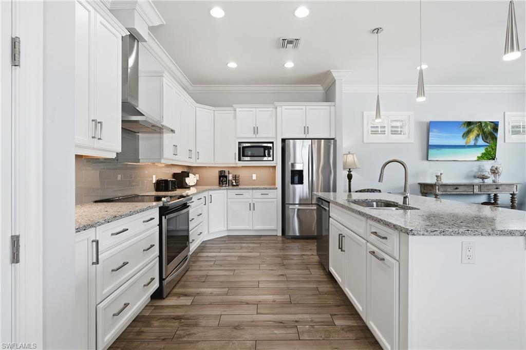Kitchen featuring white cabinetry, stainless steel appliances, granite countertops, tile backsplash, and wood-finish flooring - Virtually Edited Image