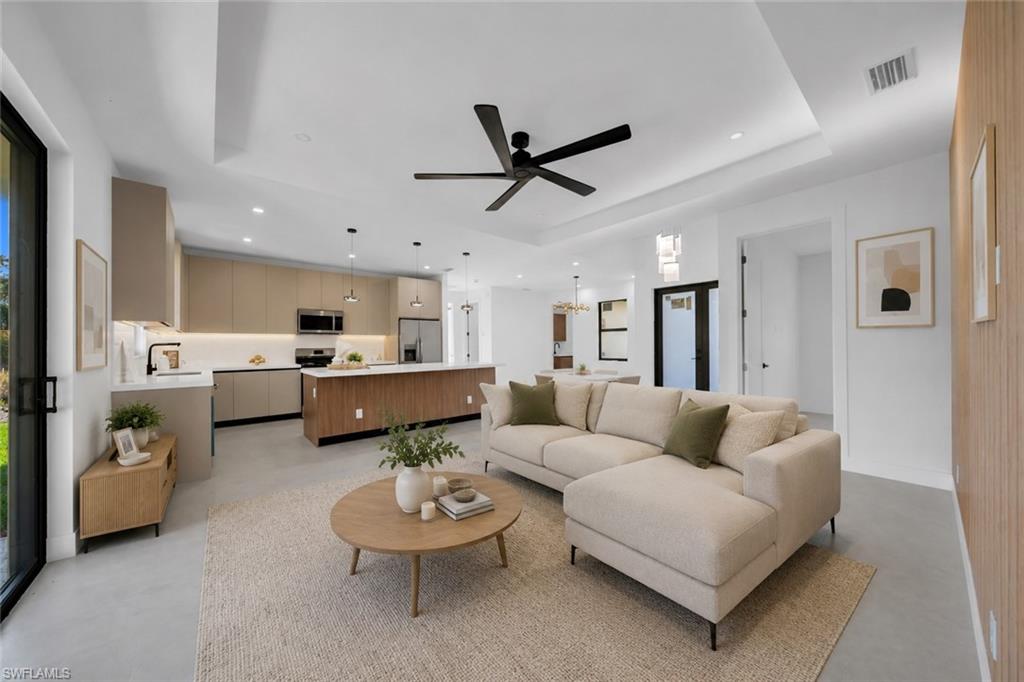 Open-concept interior featuring light-toned flooring, a tray ceiling, and a modern ceiling fan