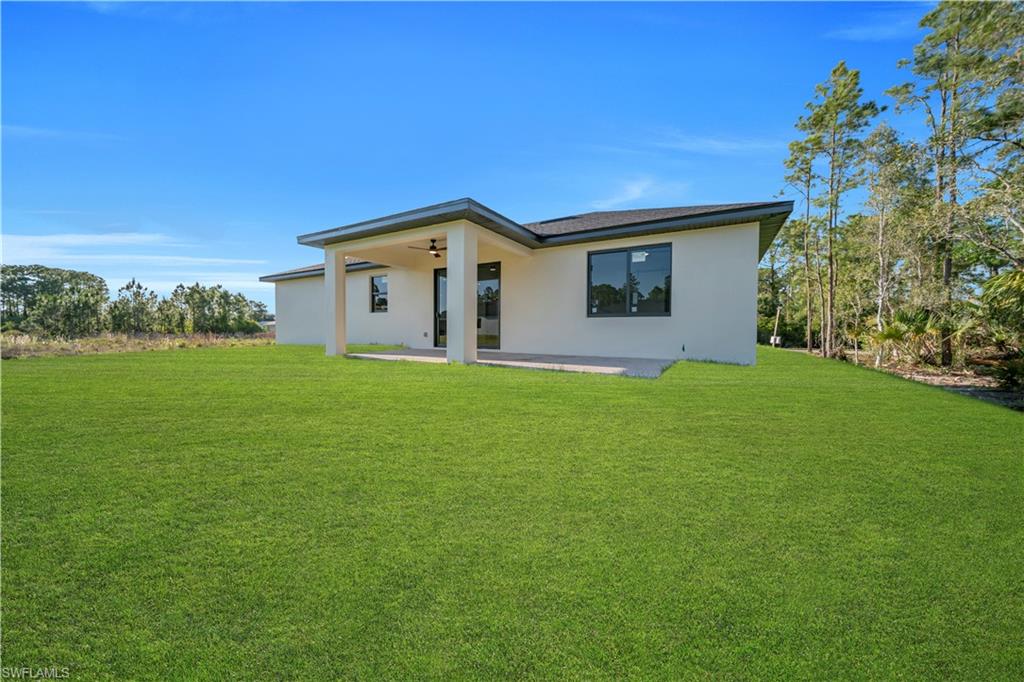 Spacious rear yard with a covered patio, featuring a ceiling fan, and ample natural light through large windows and a glass-paneled door