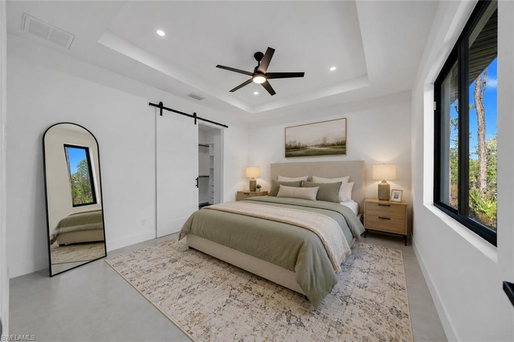 Tray ceiling with recessed lighting, ceiling fan, large window with black trim, and sliding barn door