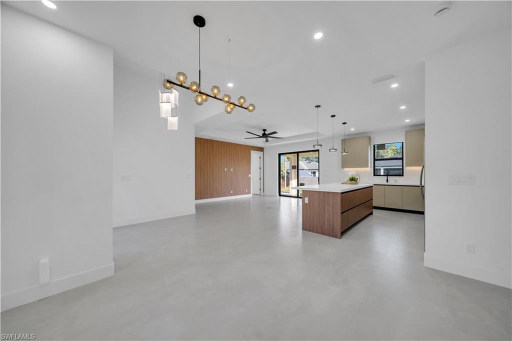 Open-concept living area with light-toned flooring, a kitchen island, and contemporary light fixtures