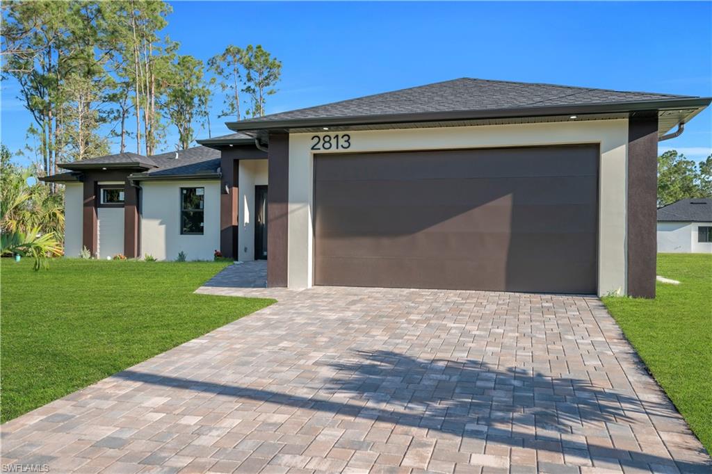 Modern exterior with a neutral stucco finish, dark accent columns, a two-car garage, and a paver driveway