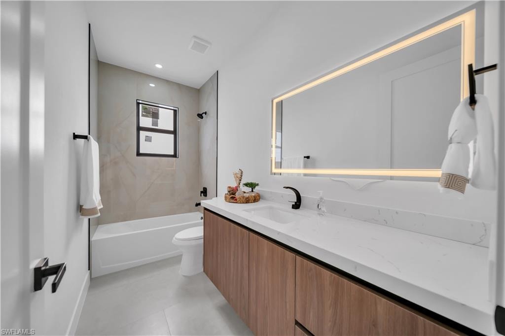 Contemporary bathroom featuring a light wood-finish vanity with an integrated white countertop, an illuminated mirror, a white bathtub, and a window with a black frame