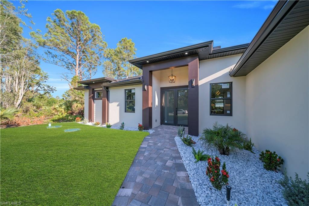 Contemporary stucco exterior with dark trim accents, paver pathway, manicured lawn, and landscaped rock beds
