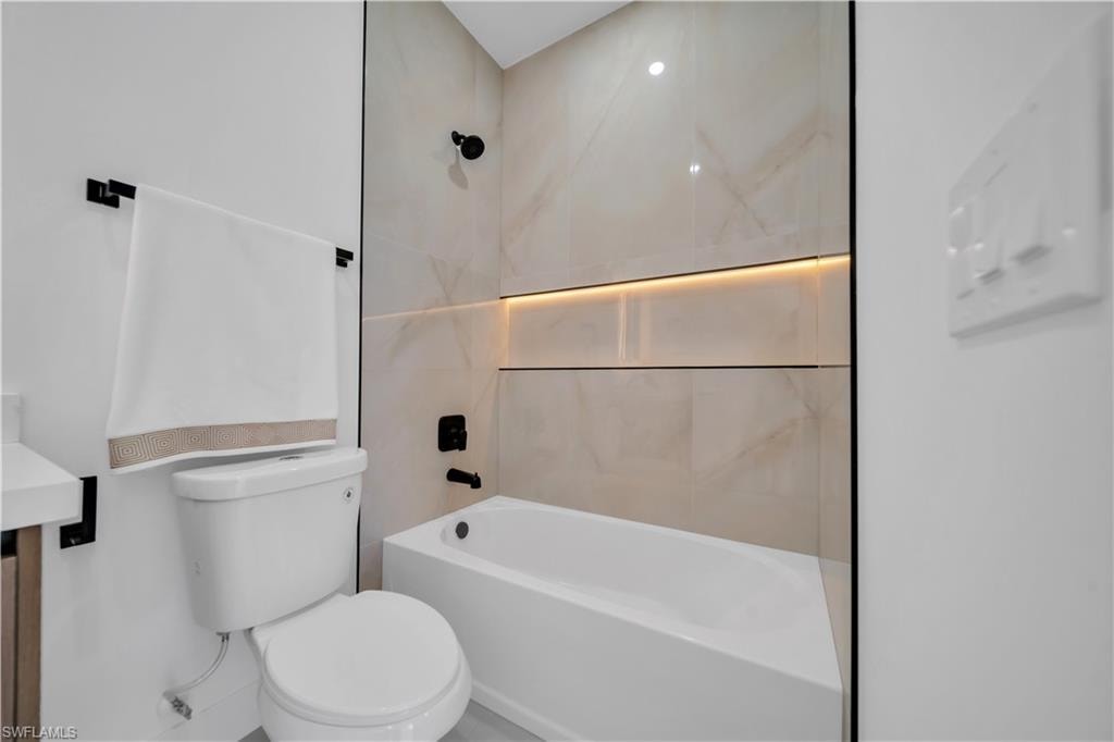 Full-height tiled shower surround with a built-in illuminated niche, matte black fixtures, and clear glass partition