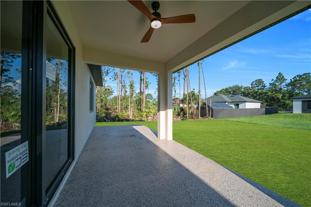 Covered patio with a wood-finish ceiling fan, expansive concrete flooring, and an open lawn space