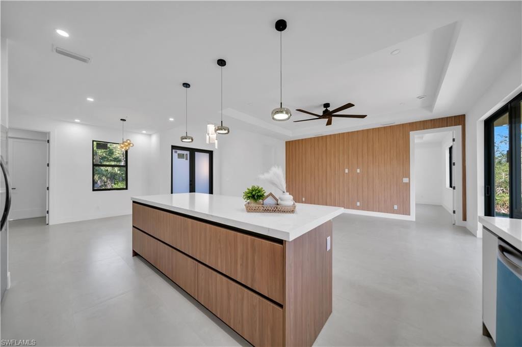 Expansive kitchen island with wood-finish cabinetry and a light-toned countertop, recessed lighting, modern pendant lighting, a ceiling fan, and a wood-paneled accent wall