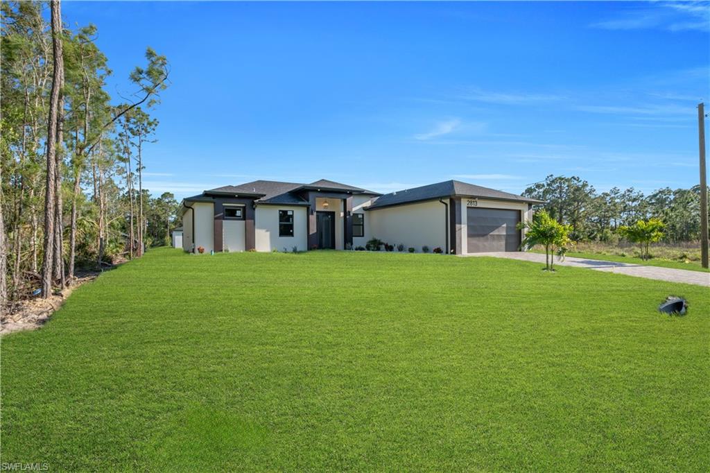 Contemporary exterior with a two-car garage, expansive green lawn, and mature trees