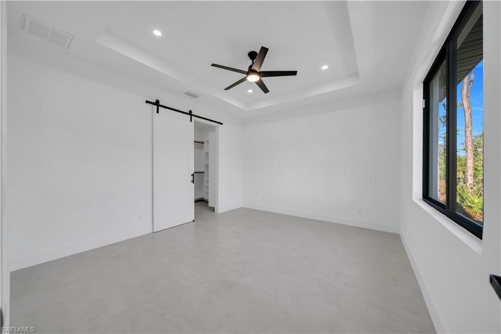 Recessed lighting and ceiling fan overhead, tray ceiling, and a barn door entry to the closet