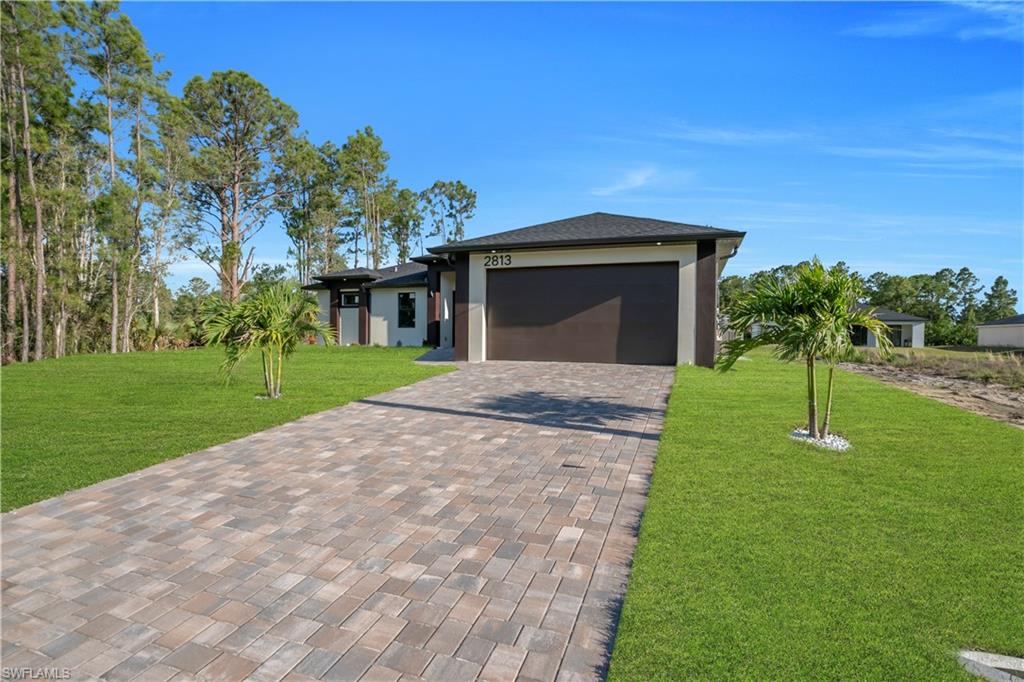Modern single-story residence with a dark brown garage door, light-toned exterior finish, and a paver driveway