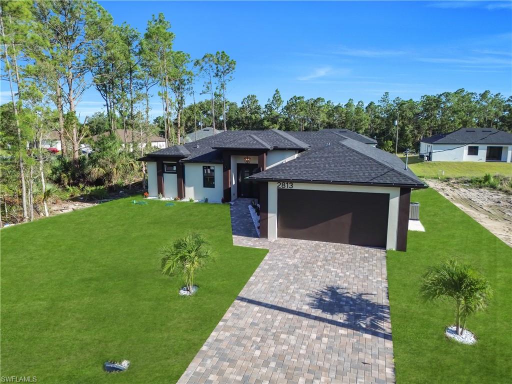 Contemporary exterior with a dark asphalt shingle roof, two palm trees, a paver driveway, and a two-car garage