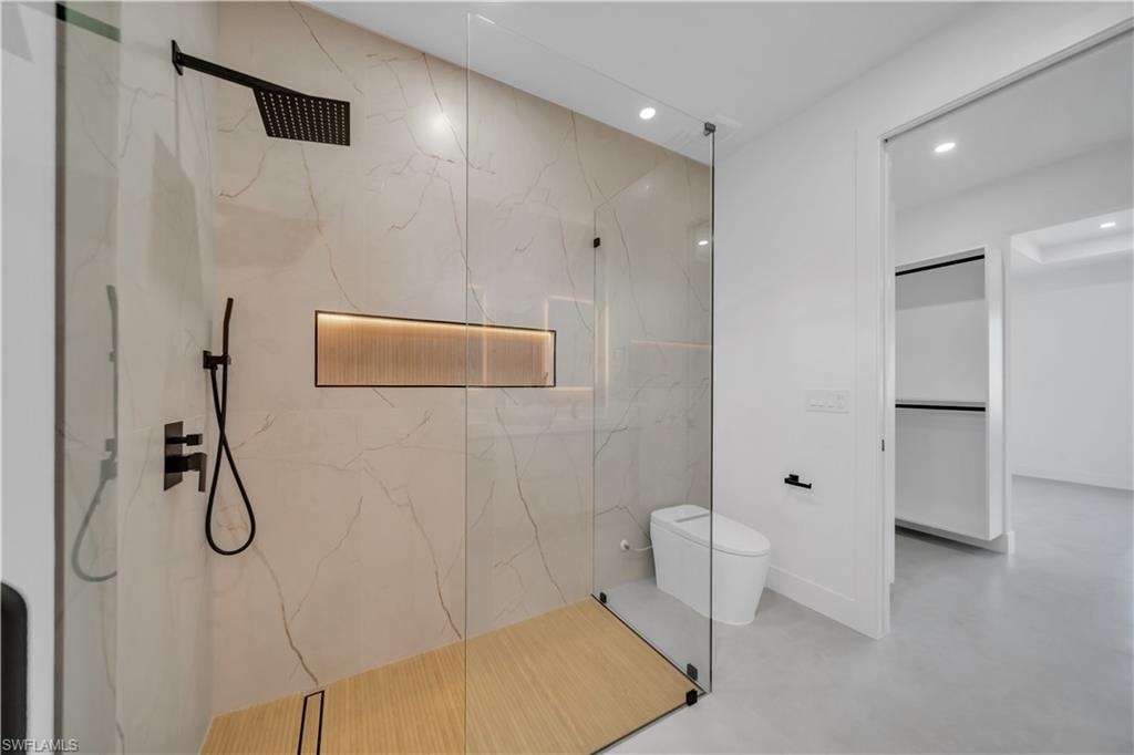 Glass-enclosed shower with a wood-finish shower pan, black matte fixtures, and an illuminated recessed niche