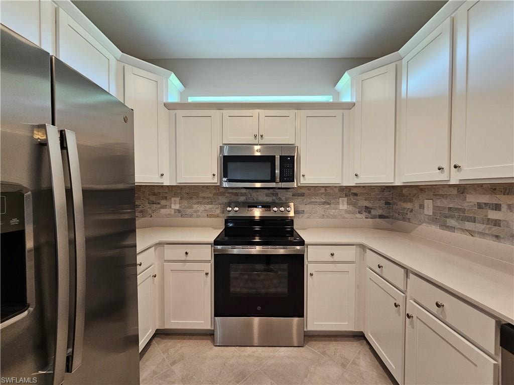 U-shaped kitchen featuring white cabinetry, stainless steel appliances, a tiled backsplash, light-toned countertops, and tiled flooring