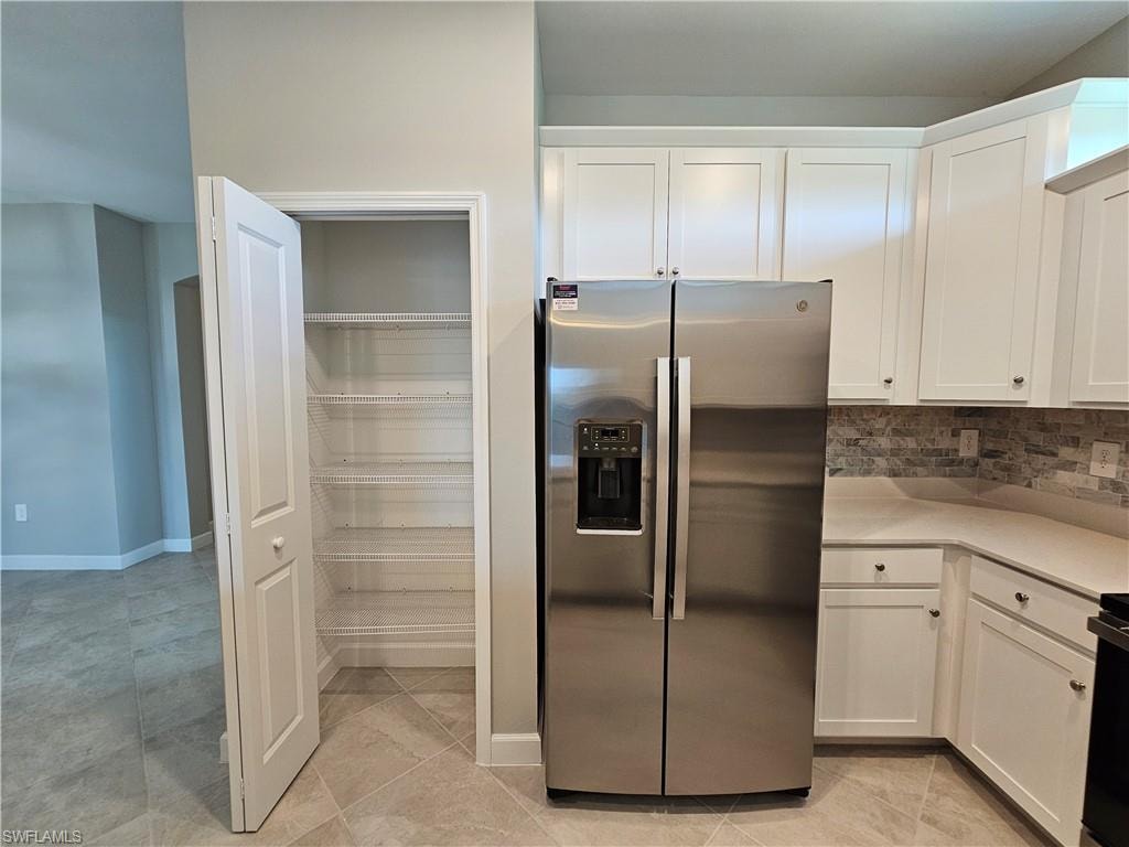 Stainless steel side-by-side refrigerator, white cabinetry, light-toned countertops, stone tile backsplash, and a pantry with wire shelving