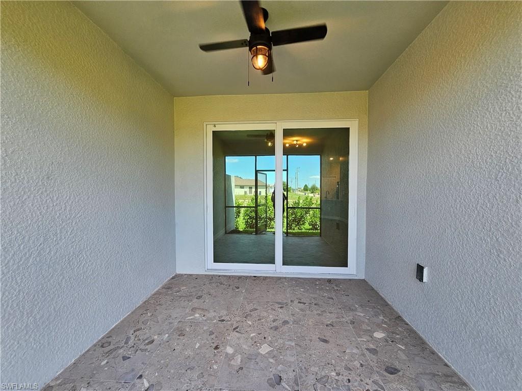 Covered patio featuring a ceiling fan with light, textured walls, and a sliding glass door