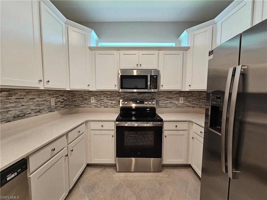 White shaker cabinetry with chrome hardware, full tile backsplash, stainless steel appliances, light-toned countertops, and large format floor tiling
