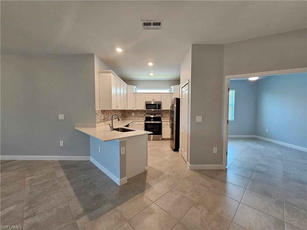 Kitchen featuring white cabinetry, stainless steel appliances, a tiled backsplash, a kitchen island with a sink, and tile flooring