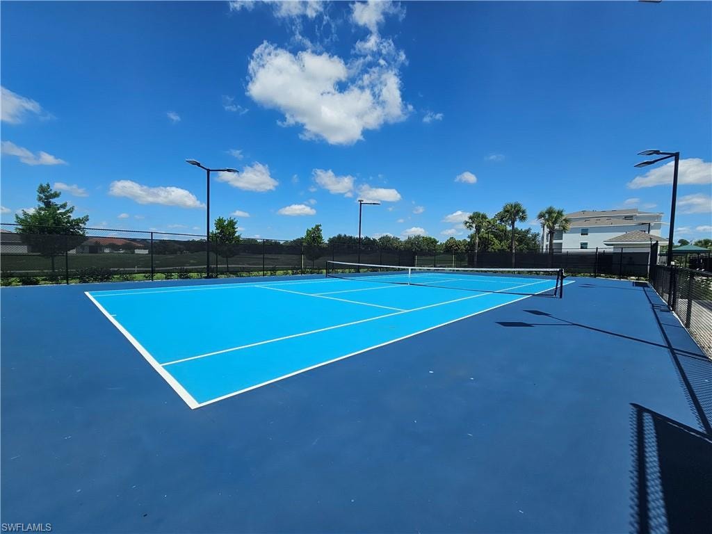 Full-size tennis court featuring a blue playing surface, white boundary lines, black perimeter fencing, and integrated lighting fixtures