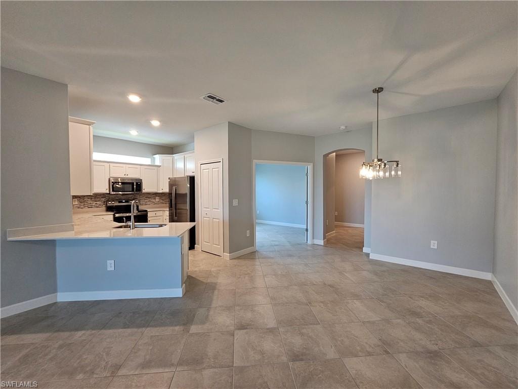 Kitchen island with an undermount sink, stainless steel faucet, white shaker cabinetry, and a mosaic tile backsplash