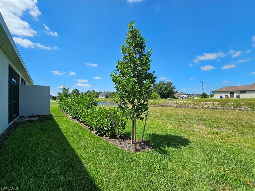 Expansive green space featuring a young tree, established shrubbery, and distant water