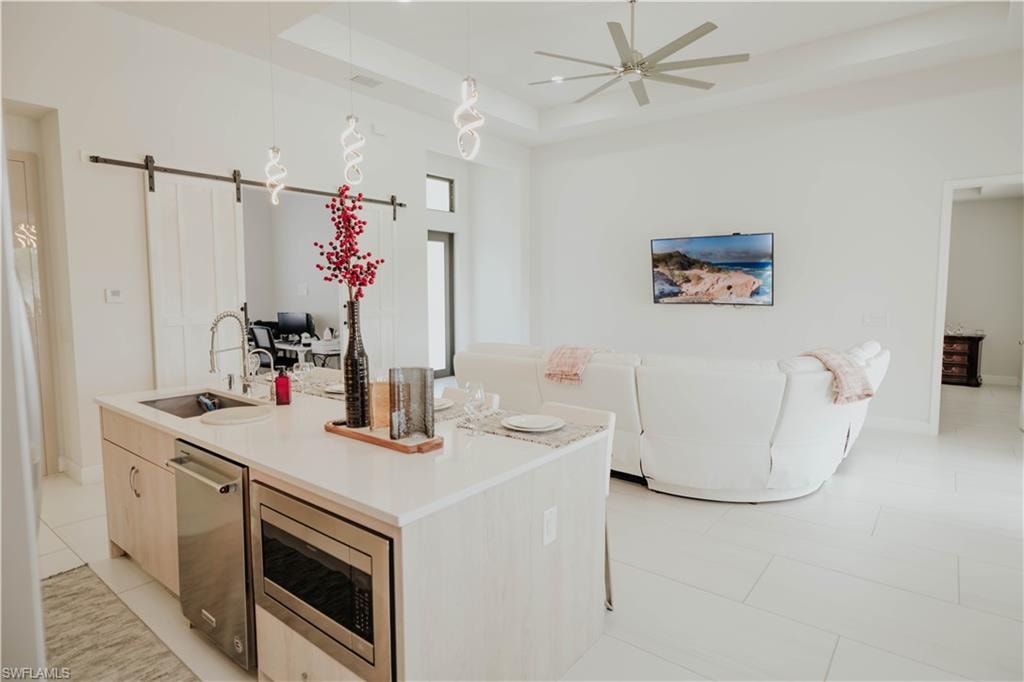 Kitchen with a barn door, a kitchen island with sink, stainless steel appliances, a sink, and hanging light fixtures