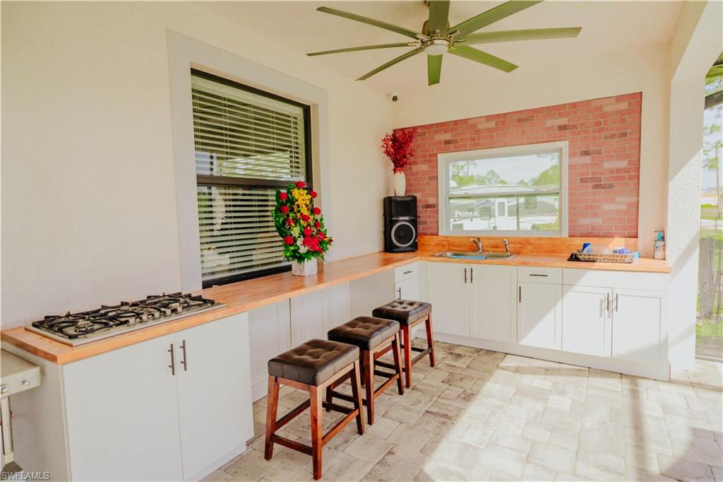 Kitchen with a ceiling fan, gas stovetop, white cabinetry, wooden counters, and a sink