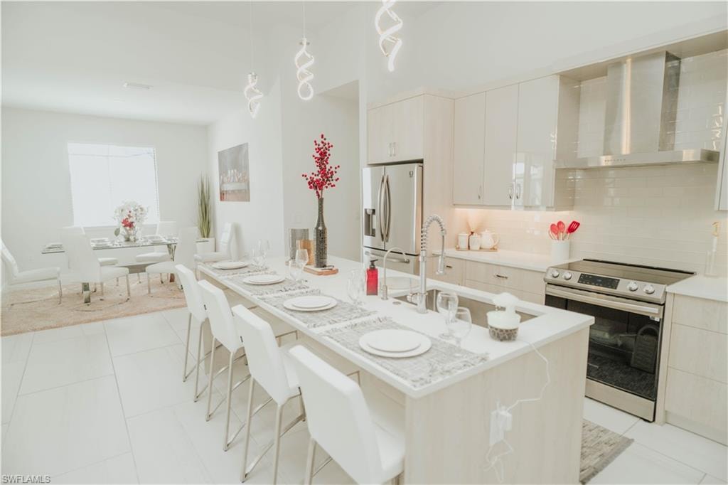 Kitchen featuring stainless steel appliances, white cabinets, light countertops, wall chimney exhaust hood, and tasteful backsplash