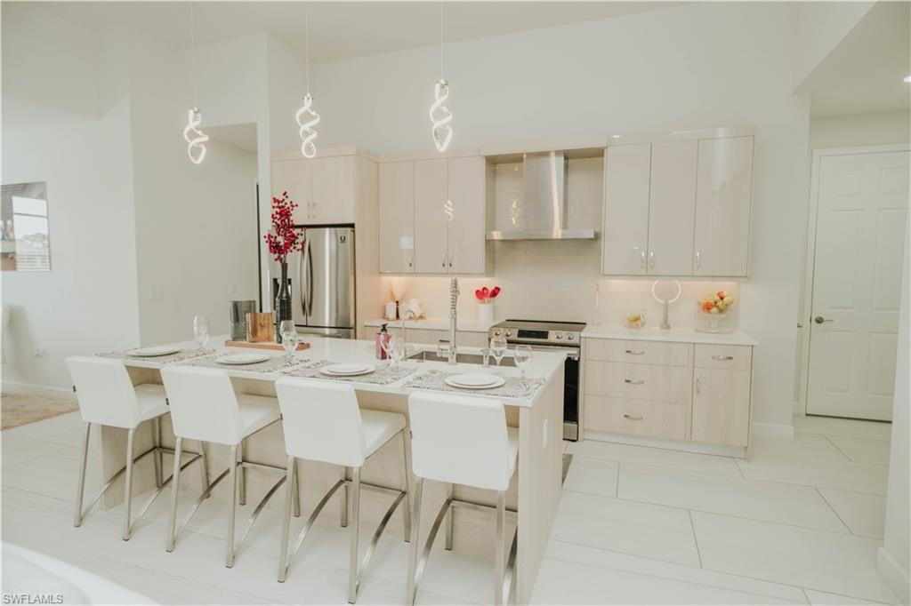 Kitchen with a kitchen island with sink, wall chimney range hood, appliances with stainless steel finishes, and decorative light fixtures