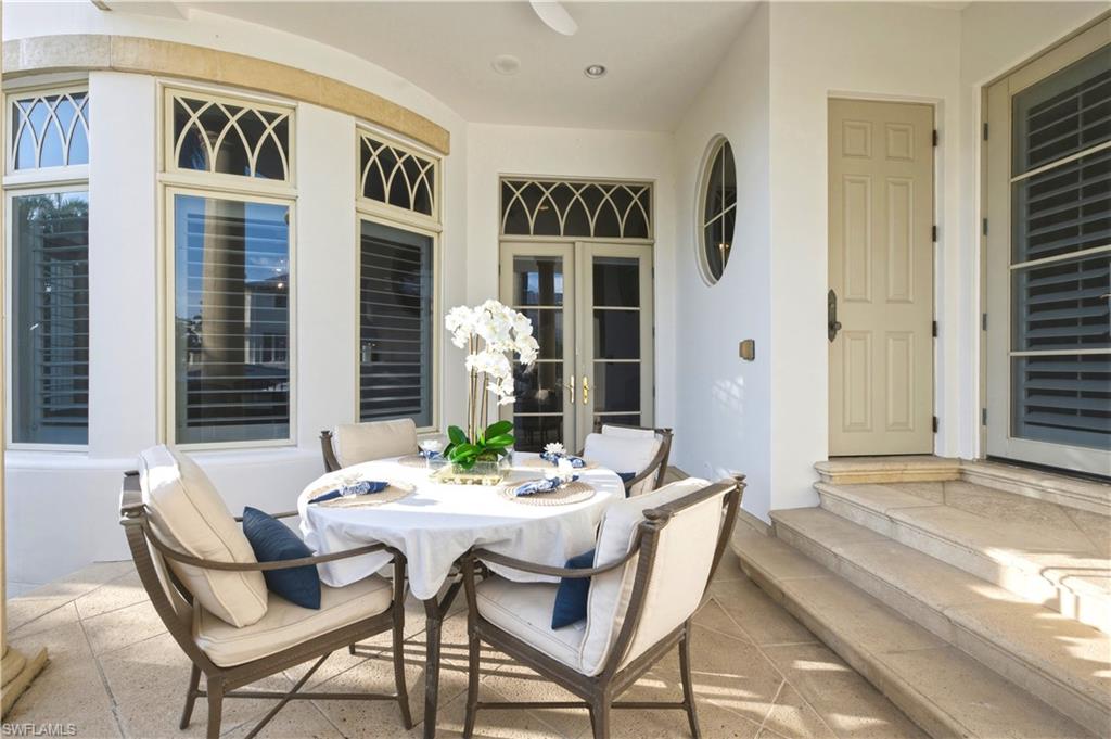 Covered lanai with decorative coffered ceiling and transom windows, furnished with a round dining table and upholstered seating