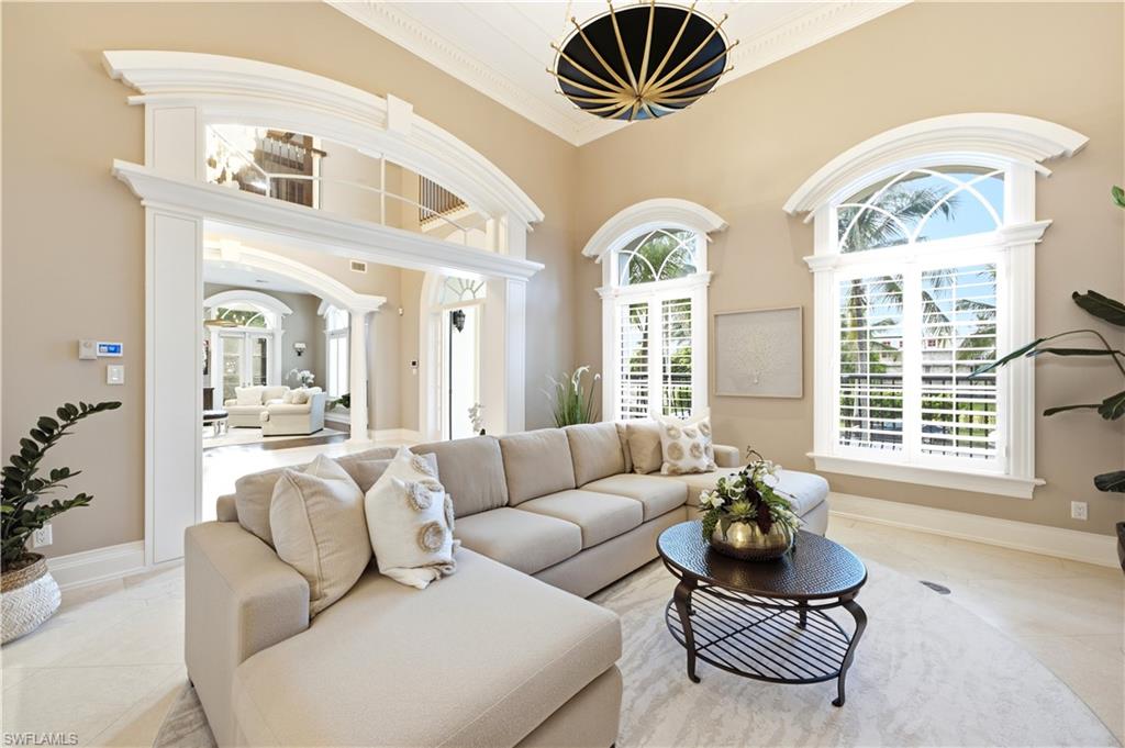 Double-height ceiling, arched windows with plantation shutters, decorative ceiling light fixture, arched entryway, and tile flooring