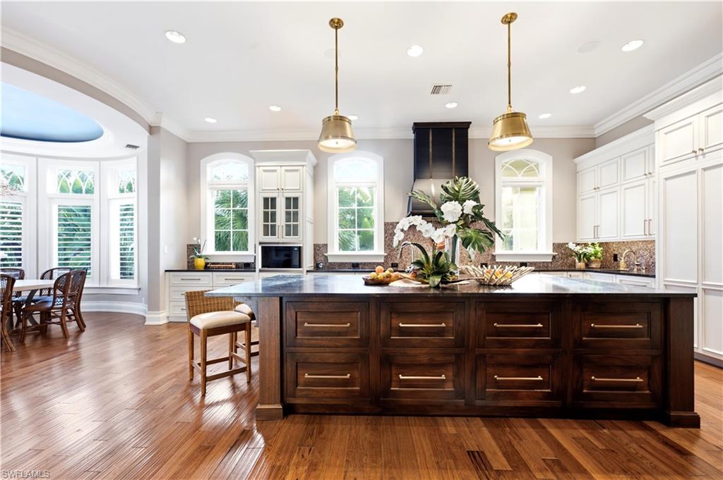 Hardwood flooring, expansive kitchen island with storage, white cabinetry, integrated range hood, and pendant lighting