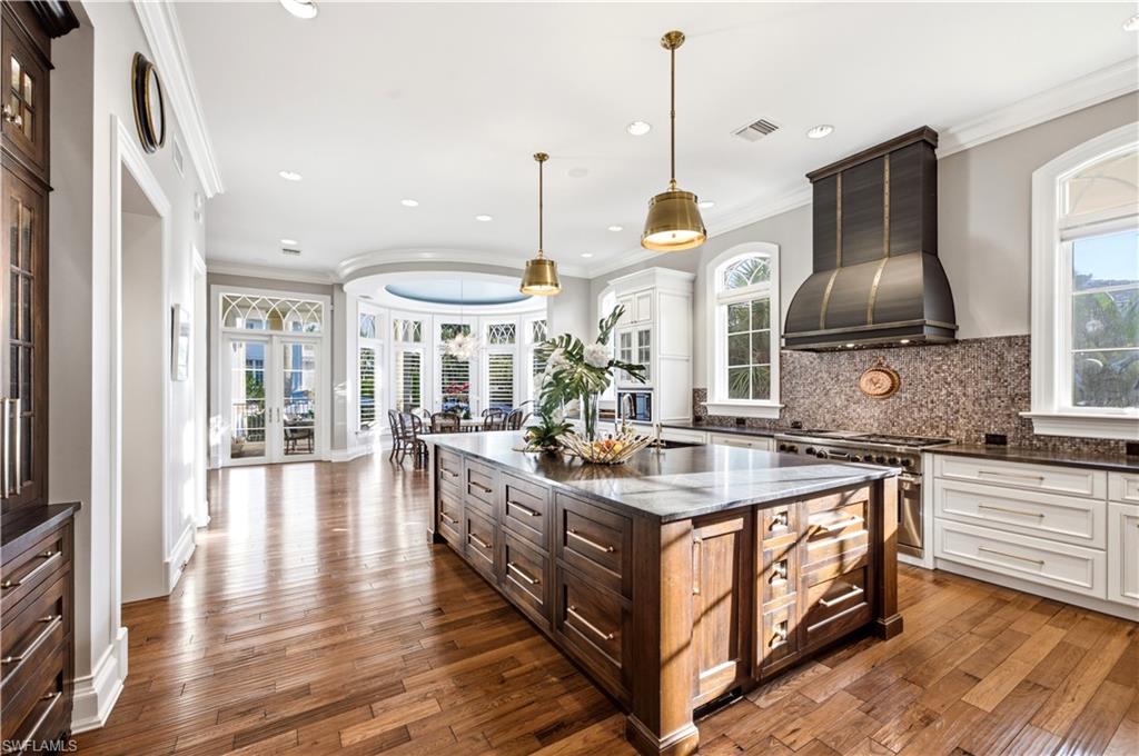Gourmet kitchen with wood-finish flooring, a large island featuring integrated storage, white perimeter cabinetry, and a custom range hood